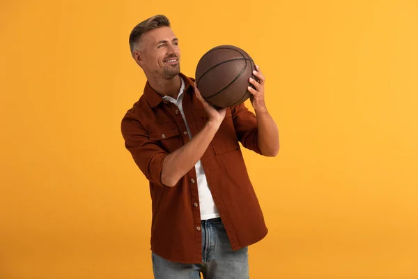 Alegre hombre sosteniendo baloncesto aislado en naranja - foto de stock