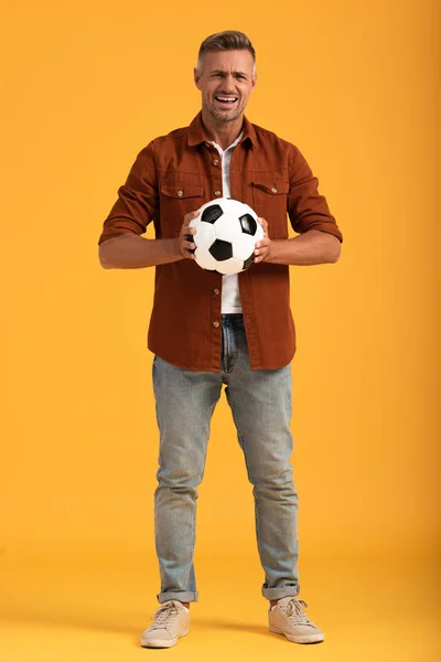 Emotionaler Mann hält Fußball in der Hand und steht auf Orange — Stockfoto