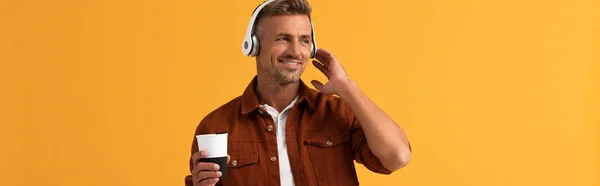 Colpo panoramico di uomo felice ascoltando musica e tenendo il caffè per andare isolato su arancione — Foto stock
