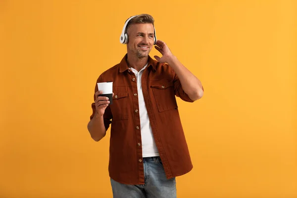 Happy man listening music and holding coffee to go isolated on orange — Stock Photo