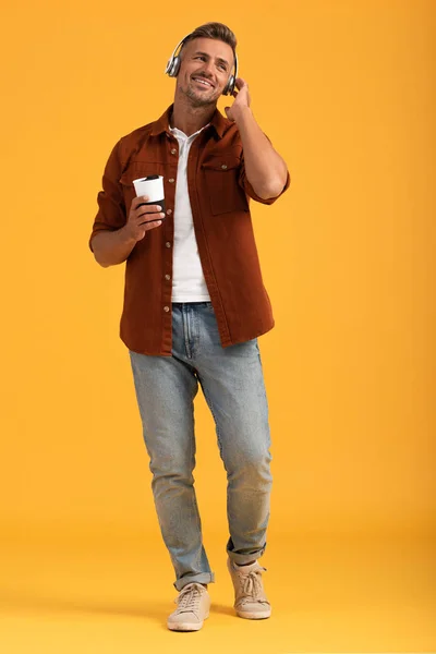 Cheerful man listening music and holding coffee to go on orange — Stock Photo