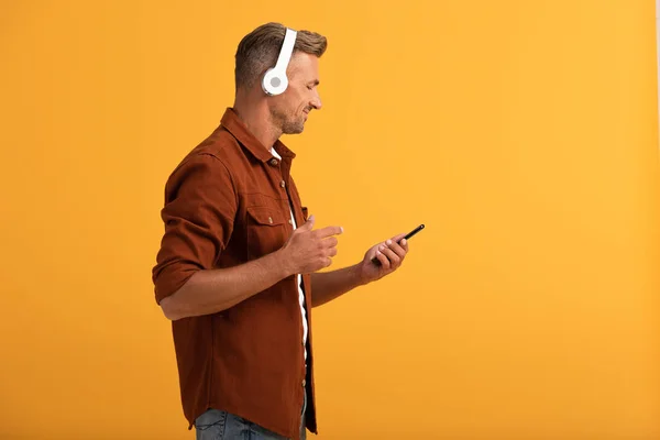 Felice uomo ascoltando musica e tenendo smartphone isolato su arancione — Foto stock