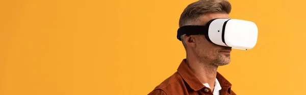 Panoramic shot of man in virtual reality headset isolated on orange — Stock Photo