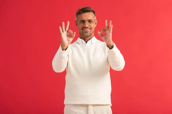 Cheerful man in glasses showing ok sign isolated on red — Stock Photo