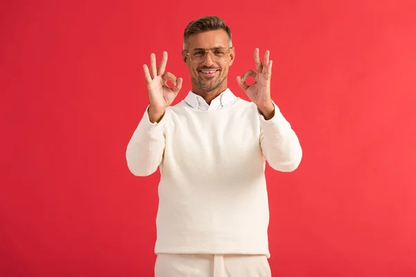 Homem alegre em óculos mostrando sinal ok isolado no vermelho — Fotografia de Stock