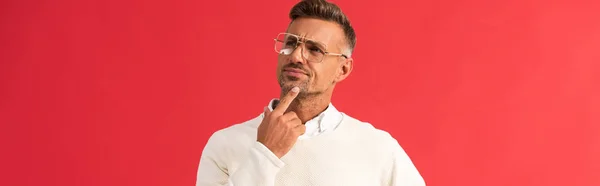 Panoramic shot of pensive man in glasses touching face isolated on red — Stock Photo