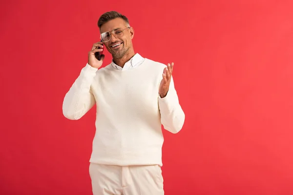 Щасливий чоловік в окулярах розмовляє на смартфоні і жестикулює ізольовано на червоному — стокове фото