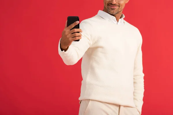 Vista recortada de hombre feliz en gafas que sostienen teléfono inteligente aislado en rojo - foto de stock