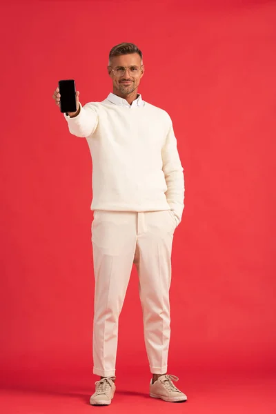 Glücklicher Mann hält Smartphone mit leerem Bildschirm, während er mit der Hand in der Tasche steht — Stockfoto