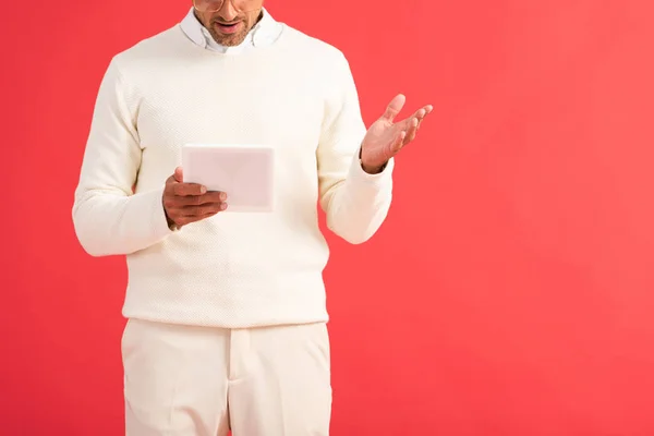 Vista ritagliata di uomo sorpreso gesticolando tenendo tablet digitale isolato sul rosso — Foto stock