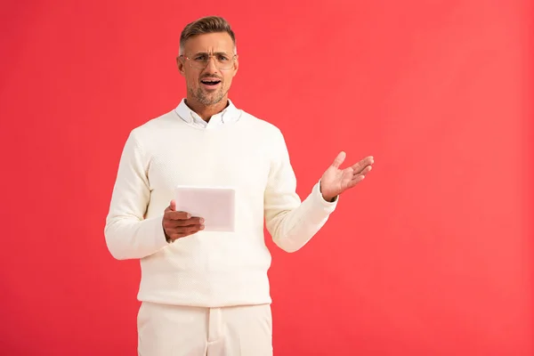 Shocked man gesturing while holding digital tablet isolated on red — Stock Photo