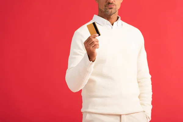 Vista recortada del hombre en posesión de la tarjeta de crédito aislado en rojo - foto de stock
