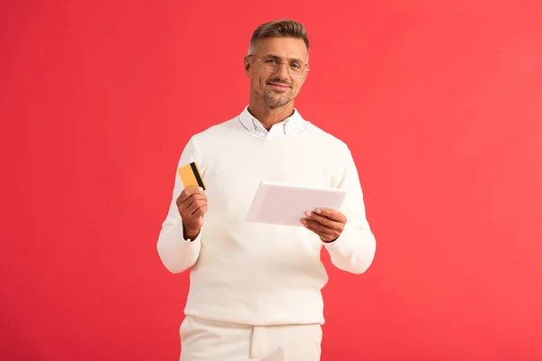 Homme heureux tenant tablette numérique et carte de crédit isolé sur rouge — Photo de stock