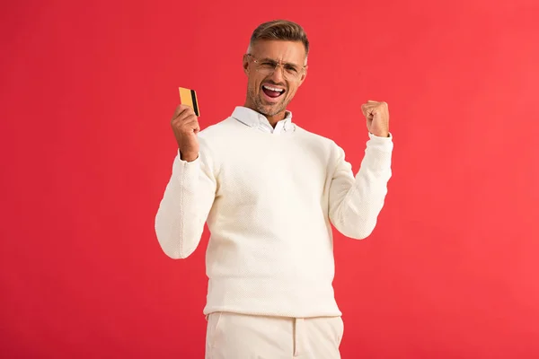 Excited man in glasses holding credit card isolated on red — Stock Photo