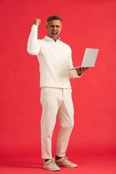 Homem animado e elegante em óculos segurando laptop no vermelho — Fotografia de Stock