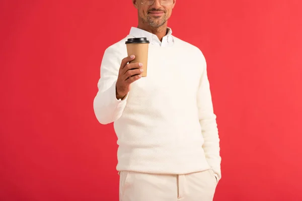 Vista recortada de hombre feliz en gafas sosteniendo taza de papel aislado en rojo - foto de stock