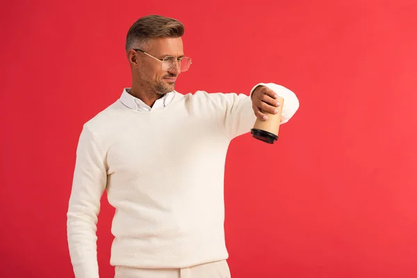 Bel homme dans des lunettes tenant tasse en papier à l'envers isolé sur rouge — Photo de stock