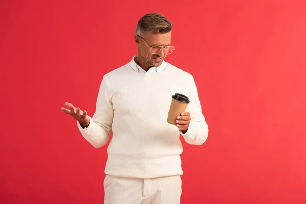 Hombre disgustado en vasos sosteniendo taza de papel aislado en rojo - foto de stock