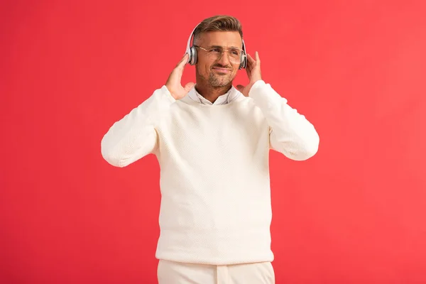 Displeased man listening music in wireless headphones isolated on red — Stock Photo