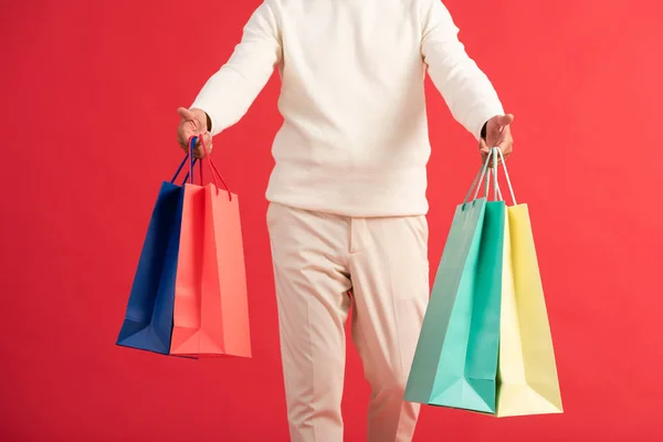 Vista cortada do homem segurando coloridos sacos de compras isolados no vermelho — Fotografia de Stock