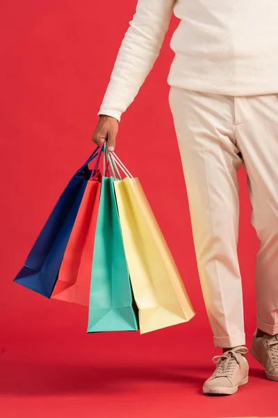 Vista recortada del hombre sosteniendo coloridas bolsas de compras aisladas en rojo - foto de stock