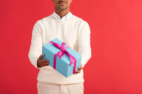 Recortado vista de sonriente hombre sosteniendo caja de regalo aislado en rojo - foto de stock