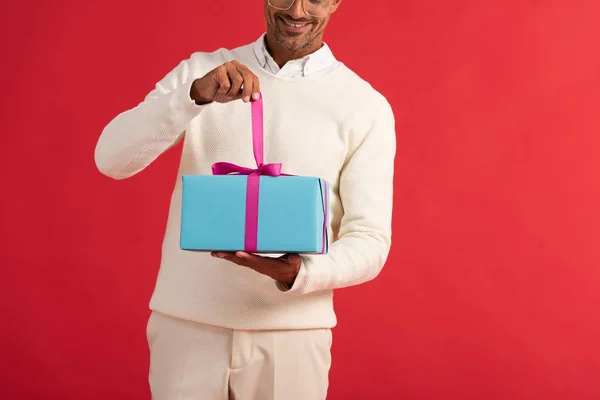 Vista recortada de hombre feliz sosteniendo caja de regalo aislado en rojo - foto de stock