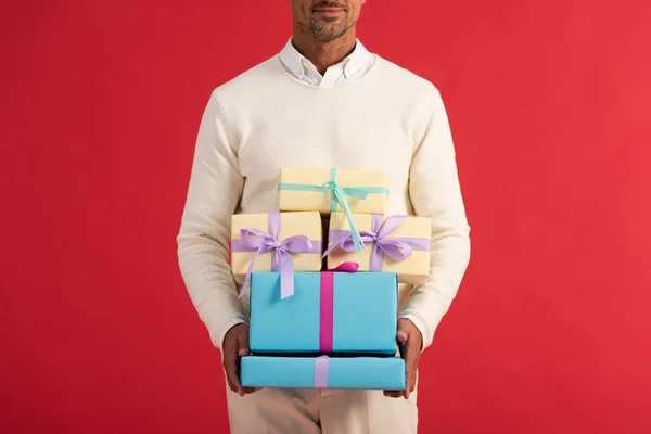 Vista recortada del hombre feliz sosteniendo cajas de regalo aisladas en rojo - foto de stock