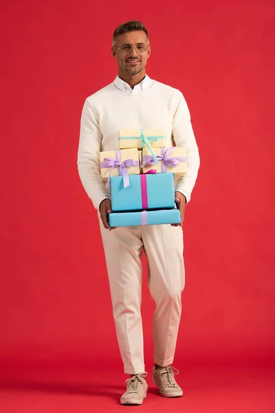 Happy man in glasses holding gift boxes while standing on red — Stock Photo