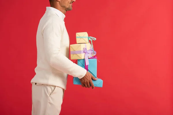 Vista recortada del hombre sonriente sosteniendo cajas de regalo aisladas en rojo - foto de stock