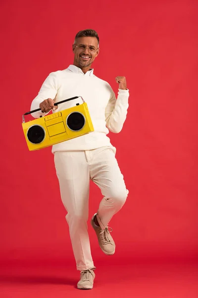 Homme positif dans des lunettes tenant boombox jaune sur rouge — Photo de stock