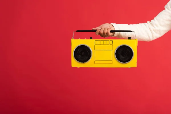 Vista ritagliata di uomo che tiene boombox giallo isolato sul rosso — Foto stock