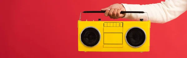 Plano panorámico del hombre sosteniendo boombox amarillo aislado en rojo - foto de stock