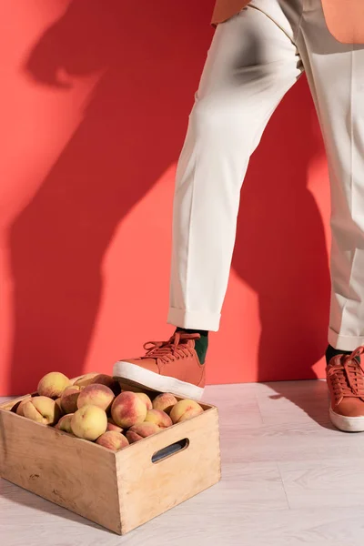 Cropped view of man standing near box with sweet peaches on red with shadows — Stock Photo