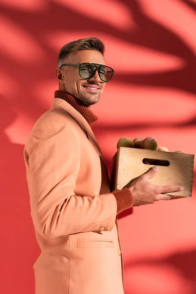 Hombre feliz en blazer y gafas de sol con melocotones dulces en rojo con sombras - foto de stock