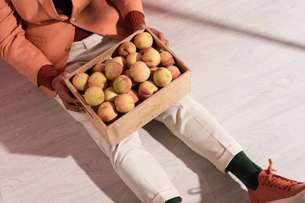 Abgeschnittene Ansicht des Mannes im Blazer sitzt mit süßen Pfirsichen in Box auf weiß mit Schatten — Stockfoto