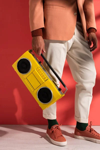 Vista ritagliata di uomo elegante che tiene boombox su rosso con ombre — Foto stock