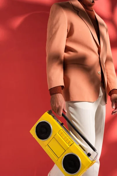 Vista cortada de homem elegante segurando boombox amarelo em vermelho com sombras — Fotografia de Stock