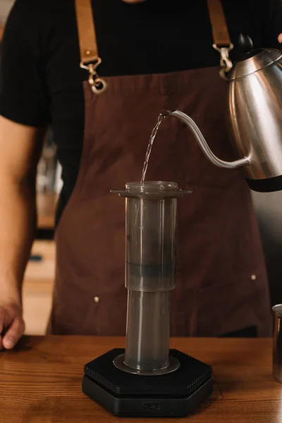 Обрезанный вид на бариста, наливающий воду из чайника в аэропрессе во время приготовления кофе — стоковое фото