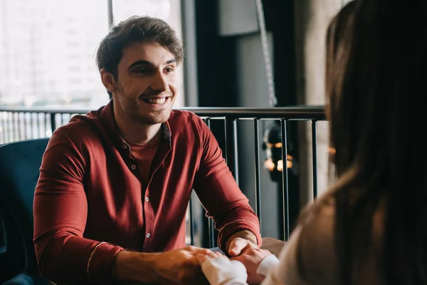 Smiling young man looking at girlfriend and holding her hands on balcony in coffee shop — Stock Photo