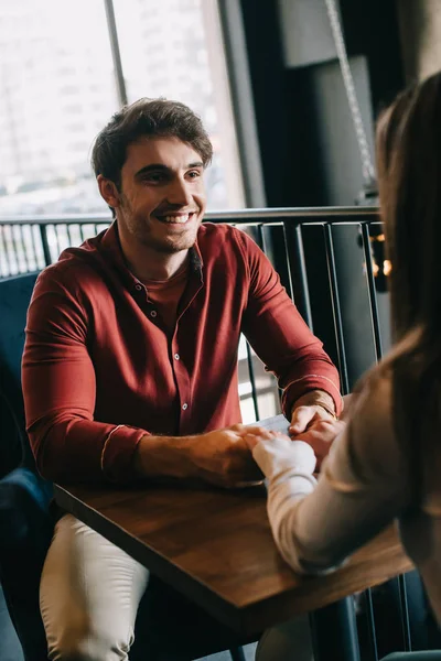Lächelnder junger Mann schaut Freundin an und hält ihre Hände auf Balkon im Café — Stockfoto