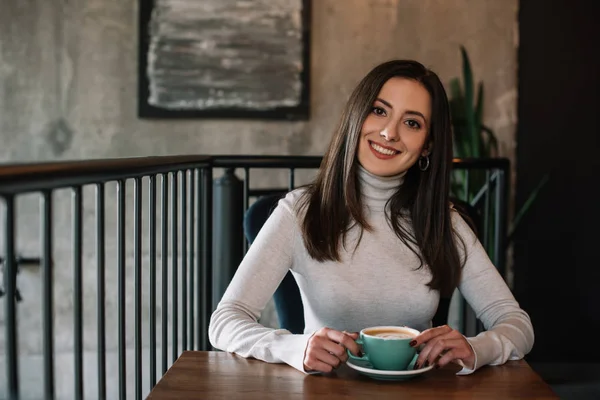 Sorrindo jovem mulher sentada à mesa de madeira com café na varanda no café — Fotografia de Stock