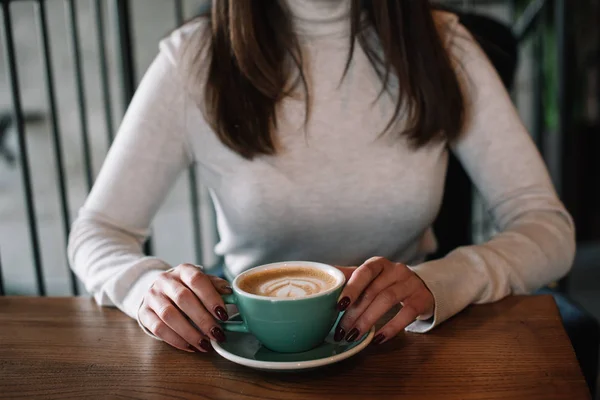 Young woman sitting at wooden table with cappuccino on balcony in coffee shop — Stock Photo