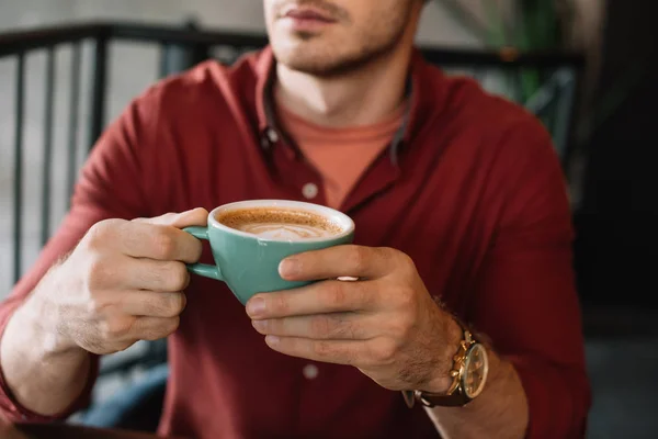 Cropped view of young man with cup of tasty cappuccino in coffee shop — Stock Photo