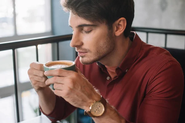 Young man smelling cappuccino with closed eyes on balcony in coffee shop — Stock Photo