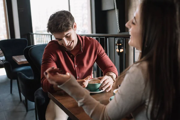 Alegre pareja hablando mientras bebe café en el balcón en la cafetería - foto de stock
