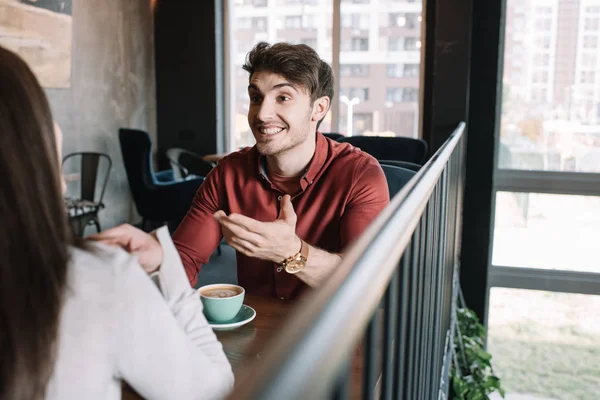 Cheerful man talking to girl while drinking coffee on balcony in coffee shop — Stock Photo