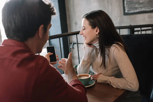 Hombre alegre que muestra la pantalla del teléfono inteligente chica mientras bebe café en el balcón en la cafetería - foto de stock