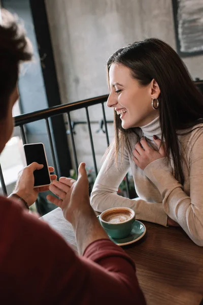 Cheerful man showing girl smartphone screen while drinking coffee on balcony in coffee shop — Stock Photo