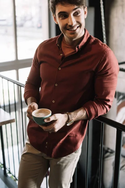 Smiling man standing on balcony with cappuccino in coffee shop — Stock Photo